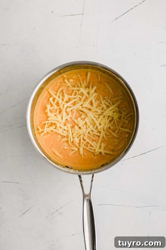Freshly shredded Monterey Jack cheese added to a small pot filled with homemade nacho cheese sauce.