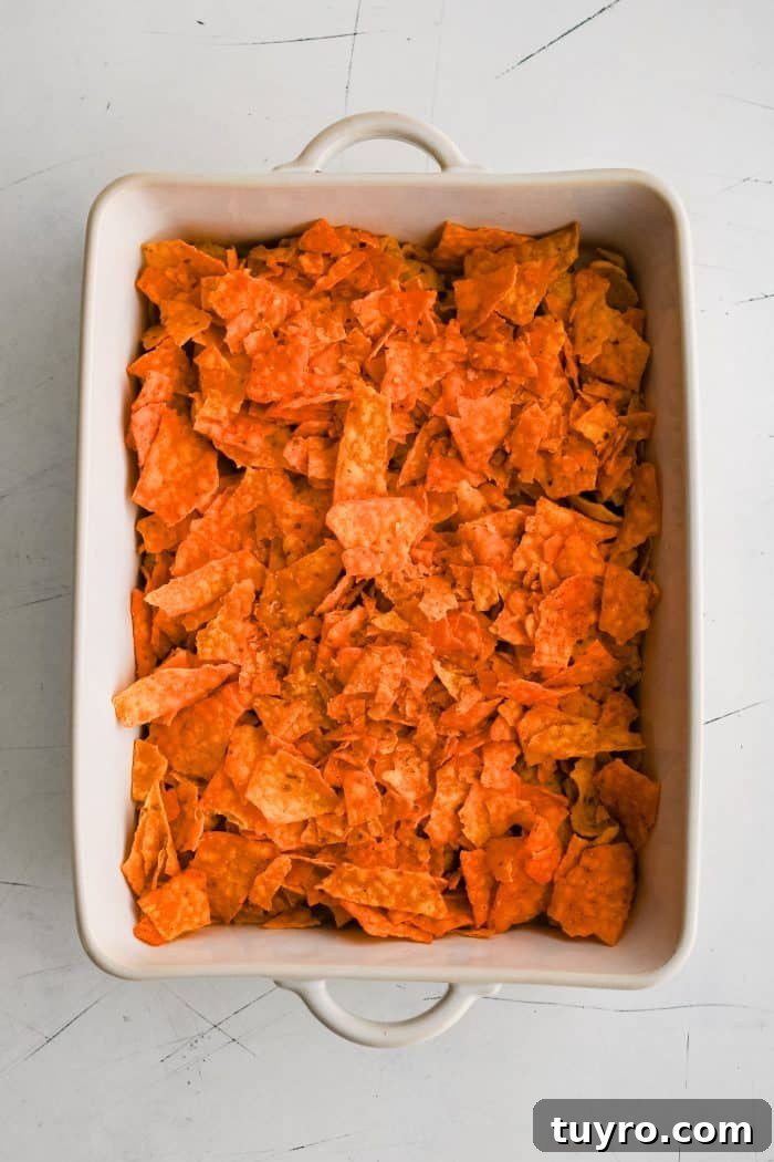 Large white ceramic casserole dish filled with a layer of Doritos on top of Fritos.