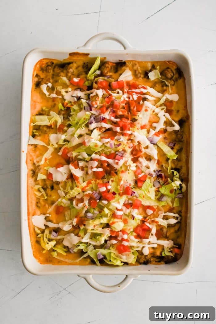 Baked walking taco casserole in a large 9x13-inch baking dish topped with shredded lettuce, tomatoes, sour cream, and hot sauce.