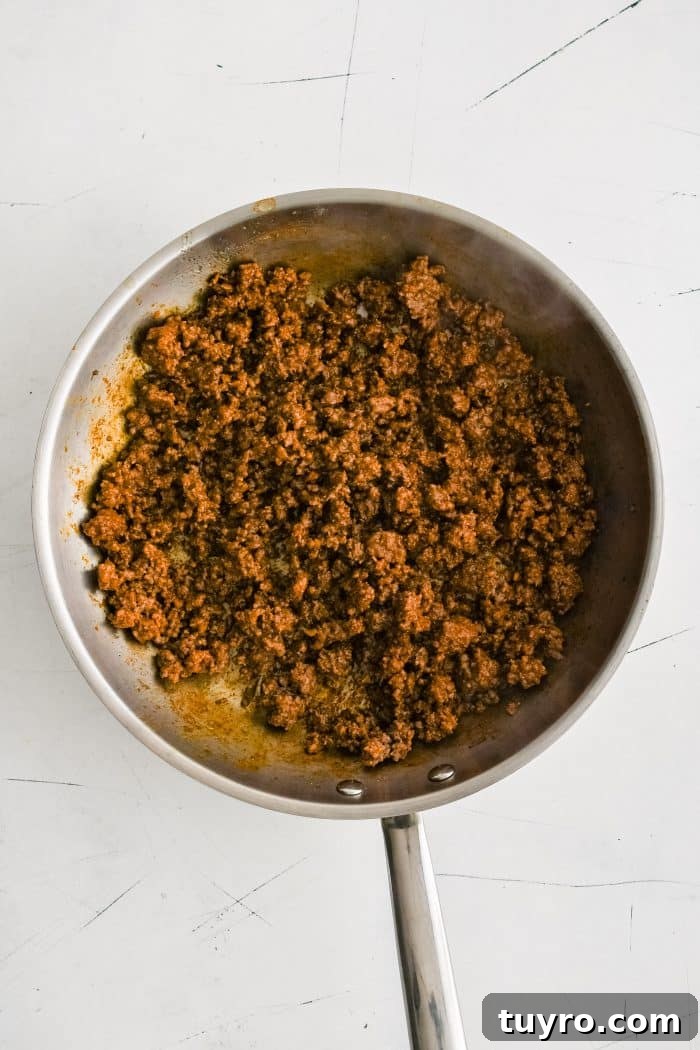 A large stainless steel skillet filled with crumbled browned ground beef seasoned with taco seasoning.
