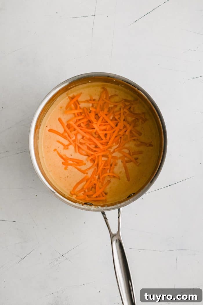Freshly shredded cheddar cheese added to a small pot filled with chili powder spiced béchamel sauce.
