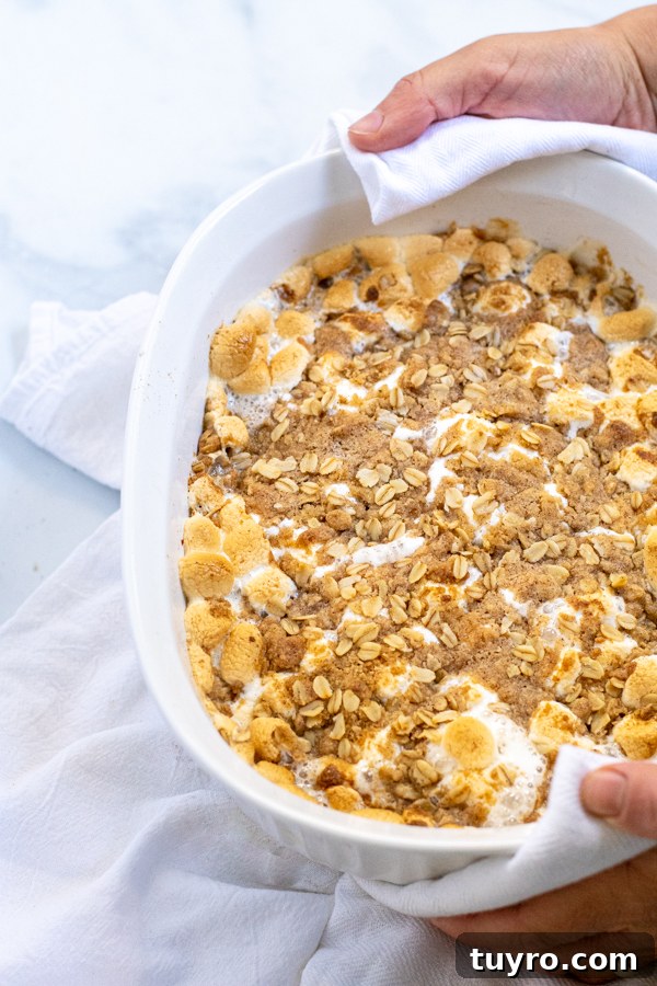 Hands holding a white baking dish with Sweet Potato Casserole with golden Marshmallows and crunchy Oat Streusel.