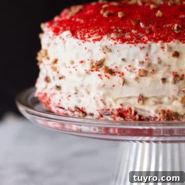 Classic Red Velvet Cake with Cream Cheese Frosting 20 Red Velvet Cake sitting on a glass cake dish, topped with cream cheese frosting and pecan chips.