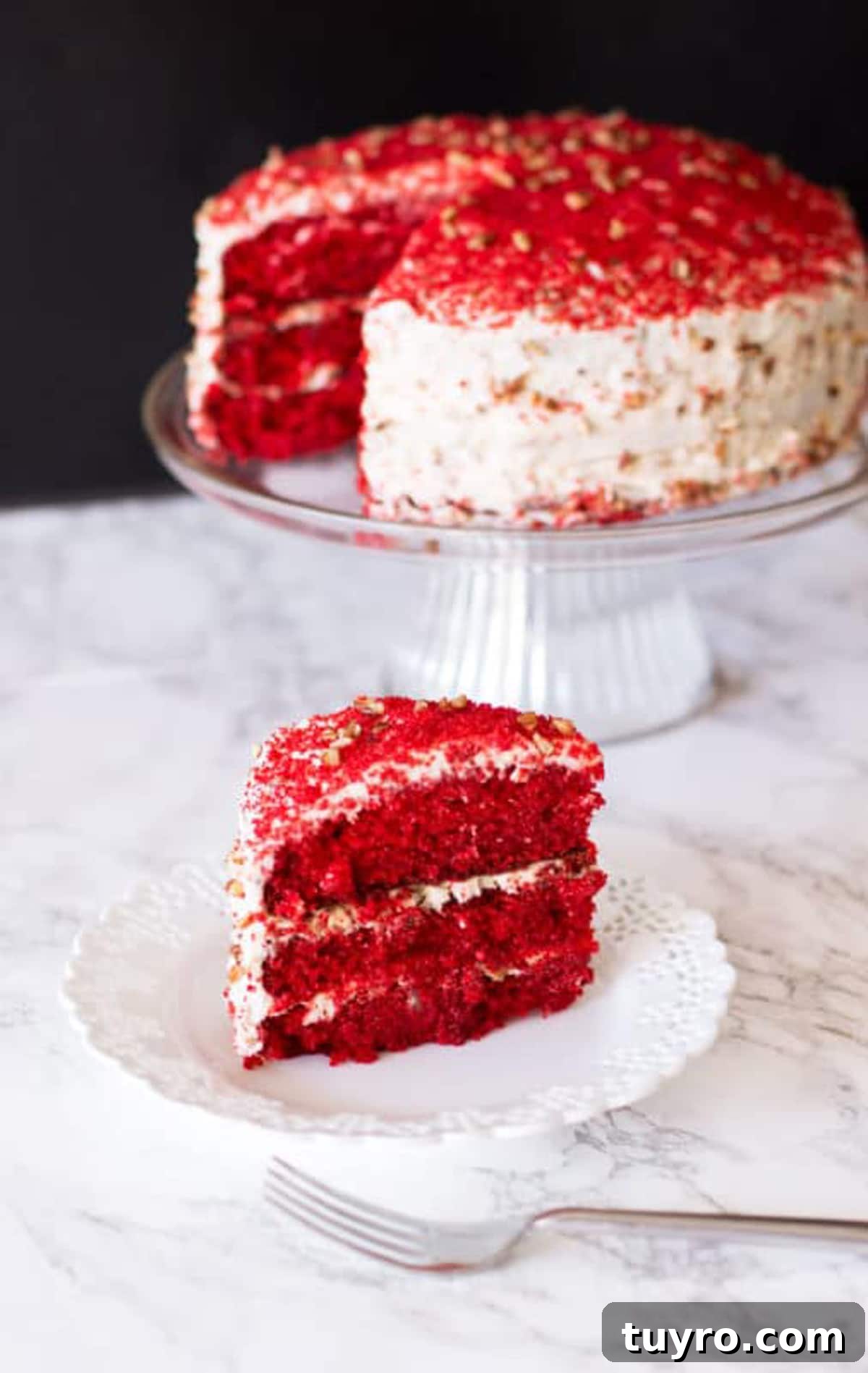 Classic Red Velvet Cake with Cream Cheese Frosting 3 Slice of Red Velvet Cake sitting on a white lace plate topped with cream cheese frosting and pecan chips, fork on table.