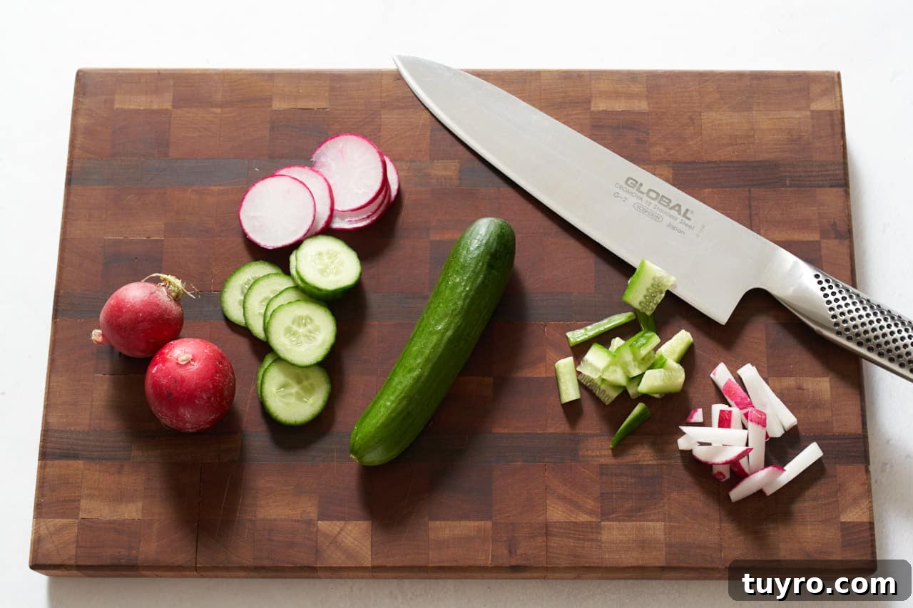 Chilled Beet Borscht: Classic Cold Soup Recipe 4 Cucumbers and radishes sliced into rounds and matchsticks on a cutting board with a knife.