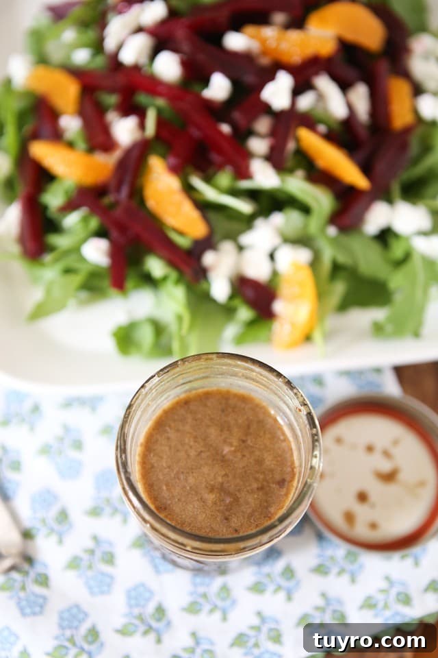 Spring Beet and Goat Cheese Arugula Salad with Walnuts mason jar of dressing next to plate of arugula salad topped with goat cheese, beet strips, orange slices, and walnuts