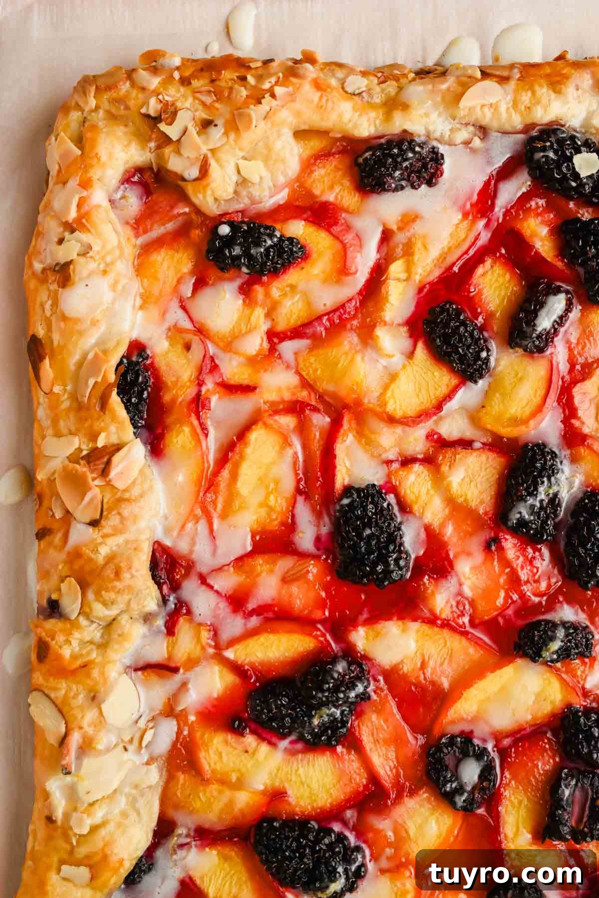 Rustic Peach and Berry Galette Recipe 2 close up corner of a peach almond croissant puff pastry galette drizzled with icing.