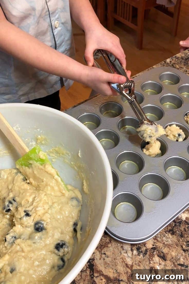 Kid-Approved Mini Blueberry Muffins Recipe 8 Scooping tablespoons of muffin batter into mini muffin tins to make blueberry muffins.